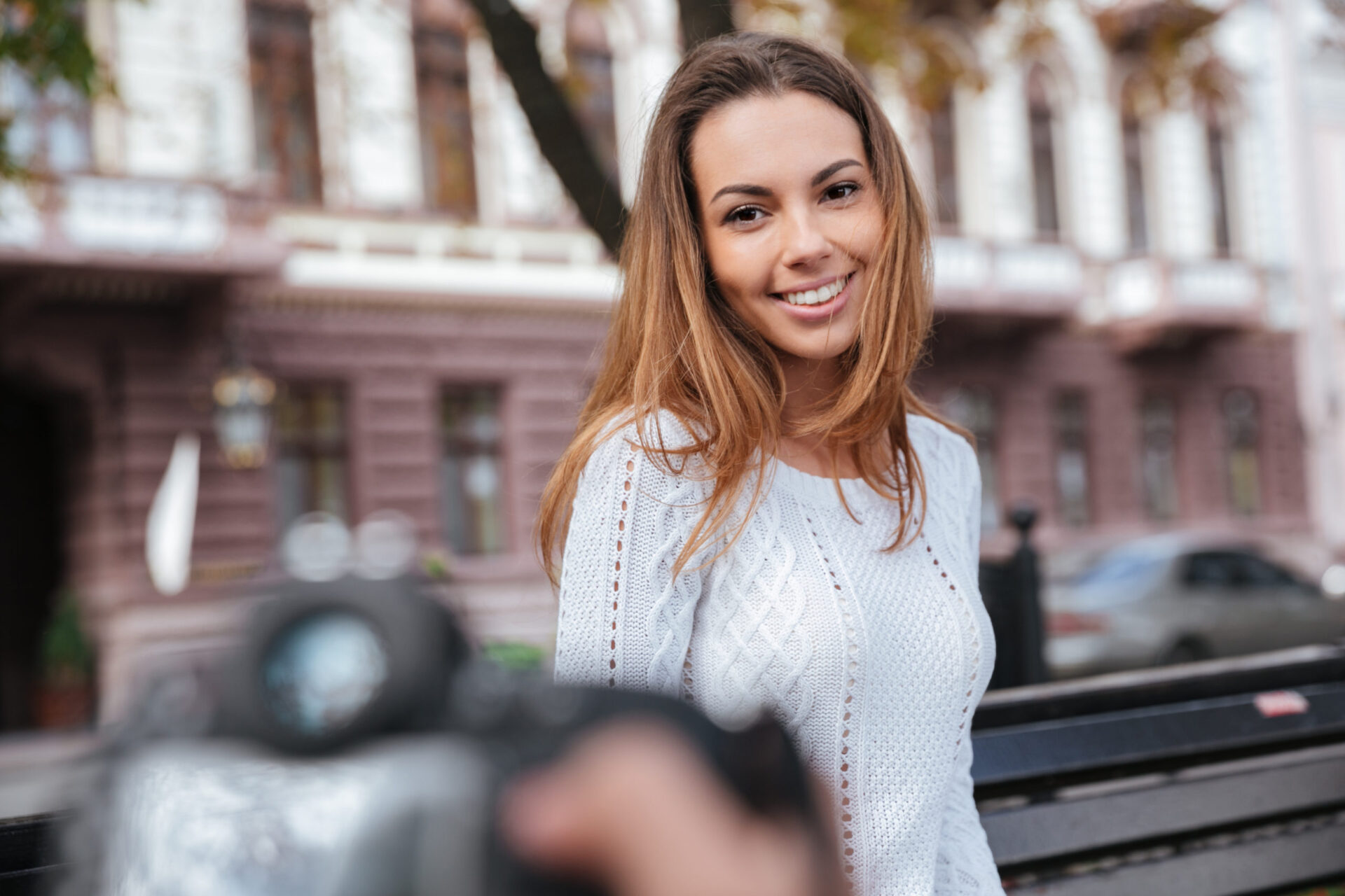 Cheerful woman sitting and posing to man photographer in park